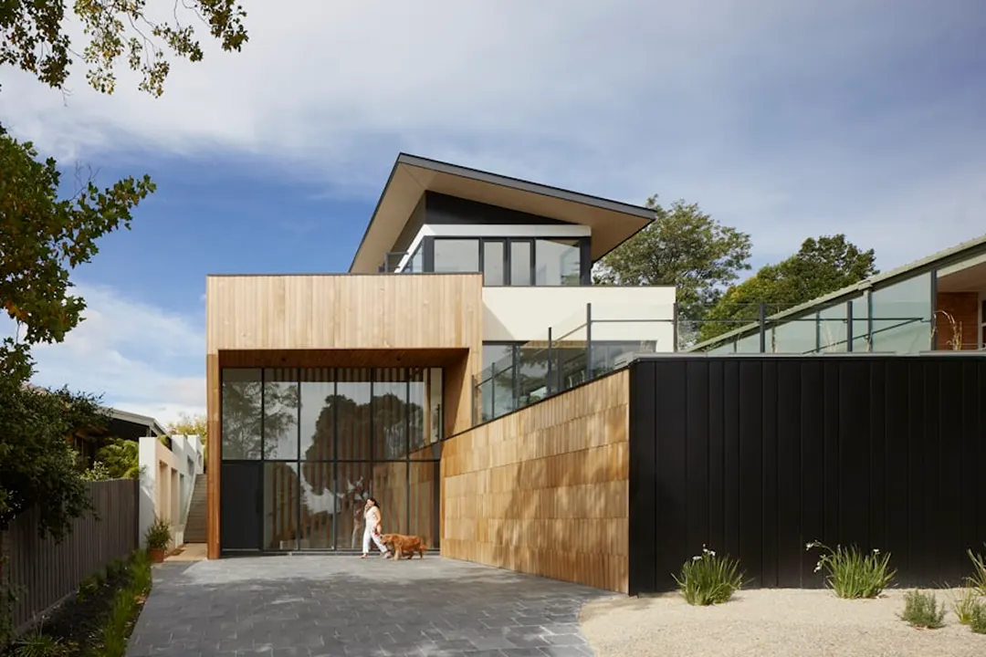 Timber-clad two-storey house with a dark fence and driveway